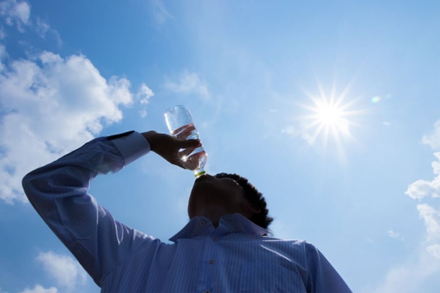 水のペットボトルを飲む長袖ワイシャツの人物