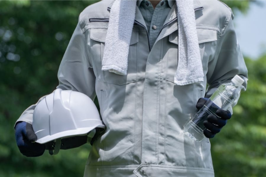 ヘルメットと水のペットボトルを持つ作業着の人物
